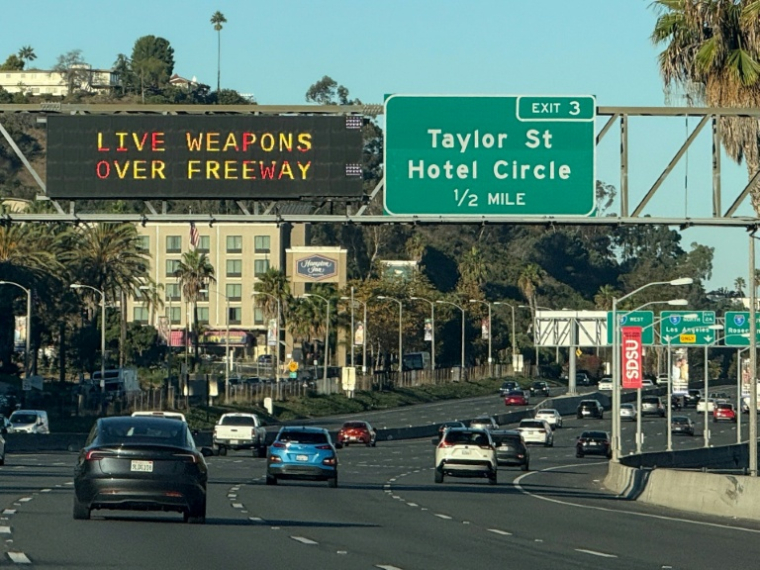 Un panneau (g) d'autoroute informe les automobilistes de la présence d'armes réelles le 18 octobre 2025 à San Diego, en Californie ( AFP / Patrick Fallon )