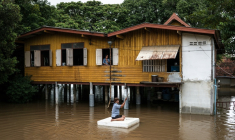 Un habitant sur un bloc en polystyrène passe en ramant devant une maison inondée dans la province d'Ayutthaya, le 6 octobre 2026 en Thaïlande ( AFP / Chanakarn LAOSARAKHAM )