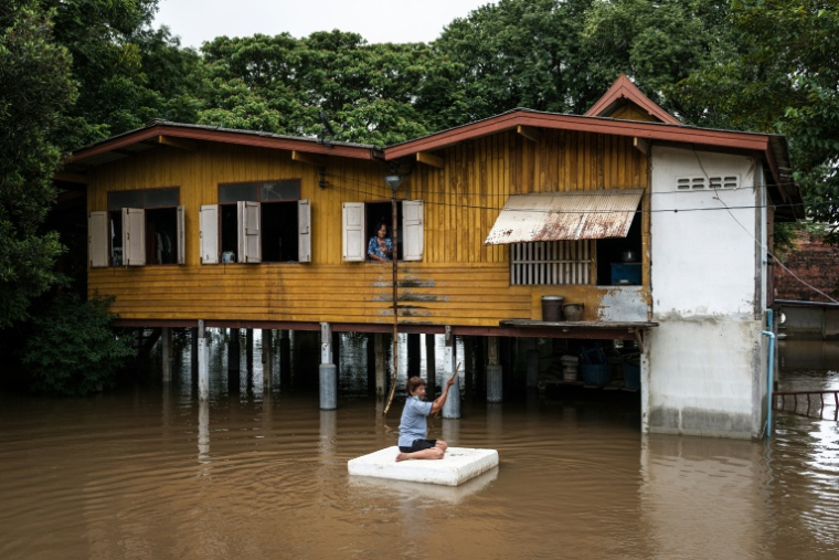Un habitant sur un bloc en polystyrène passe  en ramant devant une maison inondée dans la province d'Ayutthaya, le 6 octobre 2026 en Thaïlande ( AFP / Chanakarn LAOSARAKHAM )
