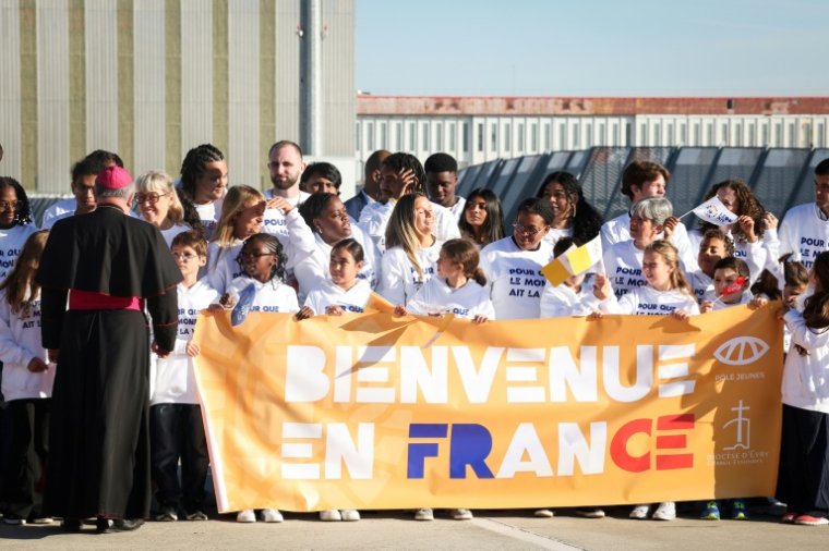 Des personnes se tiennent derrière une banderole sur laquelle on peut lire "Bienvenue en France" alors qu'elles attendent l'arrivée du pape Léon XIV devant l'aéroport d'Orly, dans la banlieue de Paris, le 25 septembre 2026 ( AFP / MEHDI FEDOUACH )