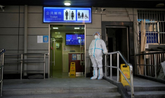 Un travailleur en combinaison de protection surveille l'extérieur d'une toilette publique à Shanghai