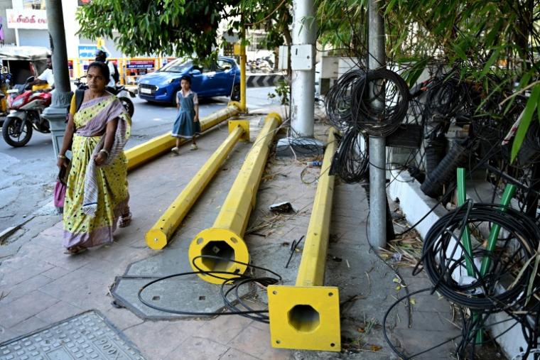 Une femme passe à côté de pylônes et de câbles sur un trottoir à Chennai, le 9 juillet 2026 en Inde  ( AFP / R.Satish BABU )