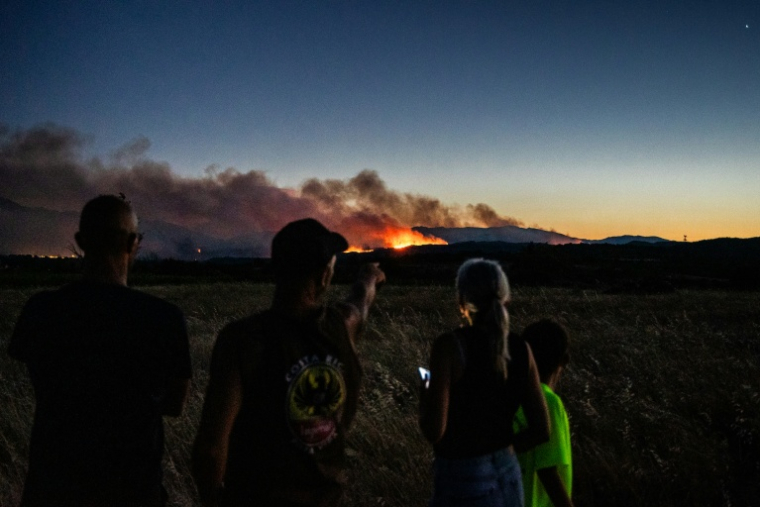 LDes habitants observent un incendie de forêt, depuis les abords de Millas, dans les Pyrénées-Orientales, le 5 juillet 2026 ( AFP / Jean-Christophe MILHET )