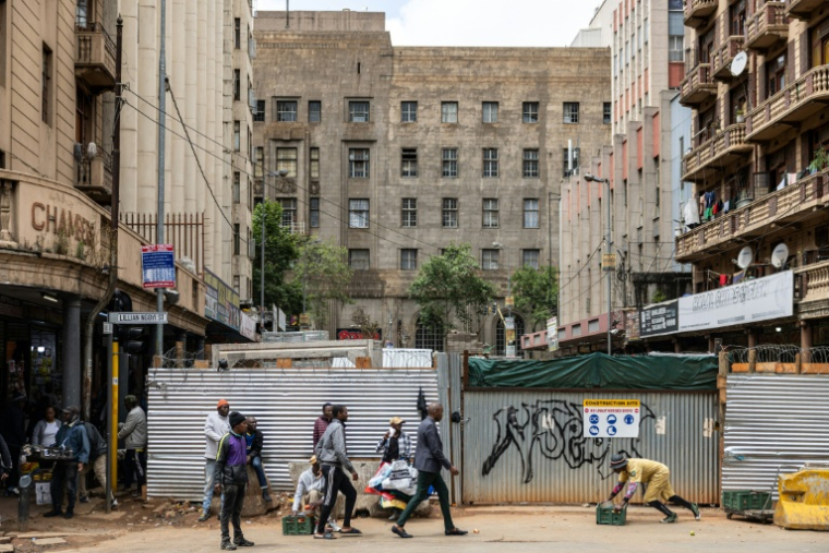 Un vendeur ambulant (à droite) pousse une caisse devant des piétons dans le quartier central des affaires de Johannesburg, le 7 novembre 2025.  ( AFP / EMMANUEL CROSET )