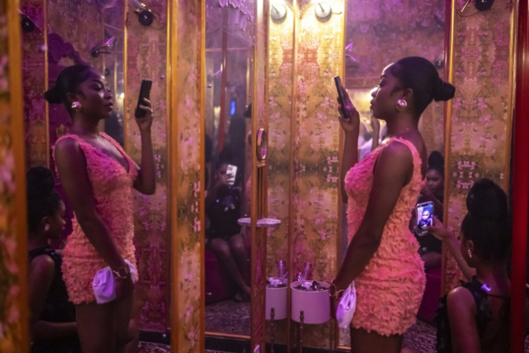 Une cliente utilise son téléphone pour se prendre en photo dans le miroir d'un espace selfie décoré dans les toilettes du restaurant et salon Zaza à Lagos, le 23 août 2025 au Nigeria ( AFP / OLYMPIA DE MAISMONT )