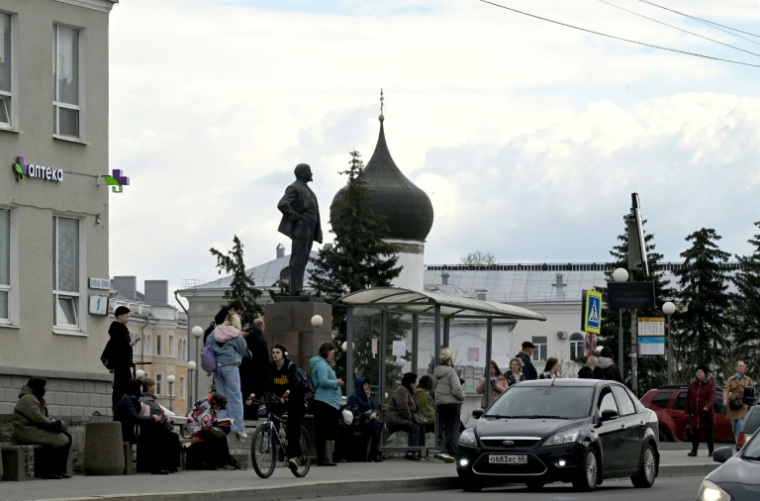 Des personnes attendent à un arrêt de bus, devant un monument dédié à Vladimir Lénine, le fondateur de l'Union soviétique, le 17 avril 2026 à Pskov, en Russie (  / Olga MALTSEVA )
