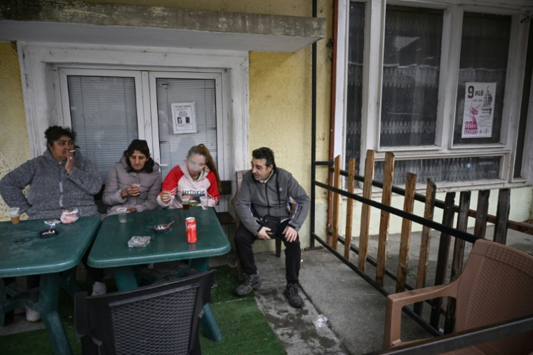 Des habitants prennent un café devant une épicerie du village de Chuprene, le 7 décembre 2025 en Bulgarie ( AFP / Nikolay DOYCHINOV )