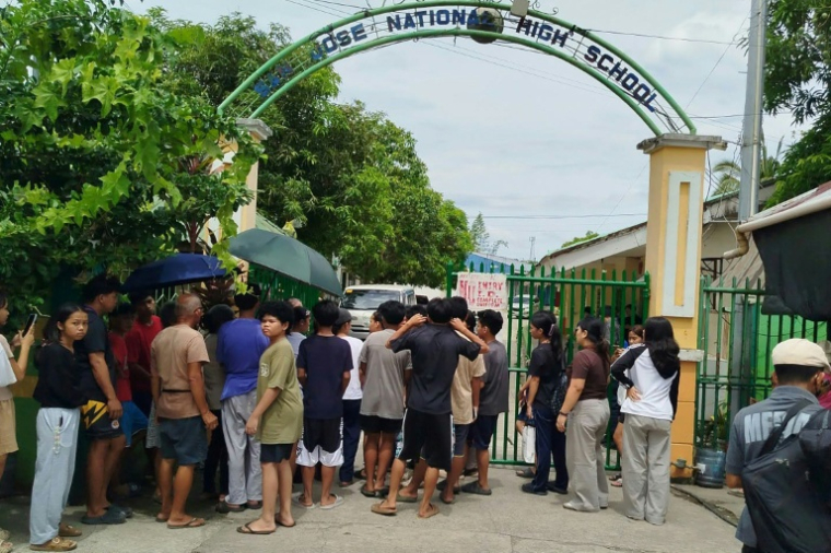 Des élèves et leurs parents attendent l'autorisation de pénétrer dans l'enceinte du lycée San José, à Tacloban, au lendemain d'une fusillade, le 23 juin 2026 aux Philippines  ( AFP / Noel  Sianosa )