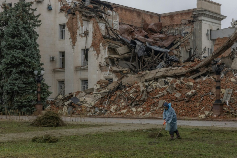 Un employé municipal ramasse de l'herbe coupée près d'un bâtiment administratif en partie détruit par une frappe russe, le 30 octobre 2026 à Kherson, dans le sud de l'Ukraine  ( AFP / Roman PILIPEY )