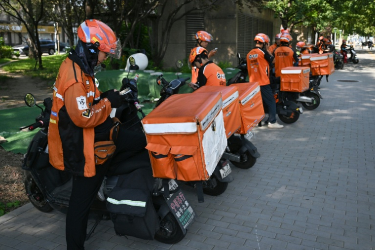 Des livreurs de repas attendent des commandes au bord d'une rue à Pékin, le 2 septembre 2026 ( AFP / Pedro PARDO )
