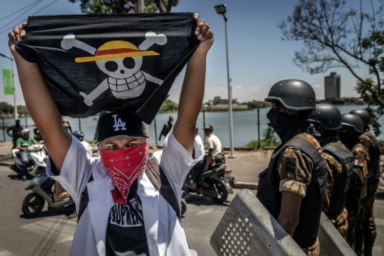 Un drapeau portant le logo du célèbre manga japonais One Piece, symbole adopté par les mouvements de protestation de la génération Z dans le monde entier, devant les forces de sécurité lors d'une manifestation exigeant de meilleures conditions de santé et des réformes constitutionnelles à Antananarivo, le 7 octobre 2025 à Madagascar ( AFP / Luis TATO )