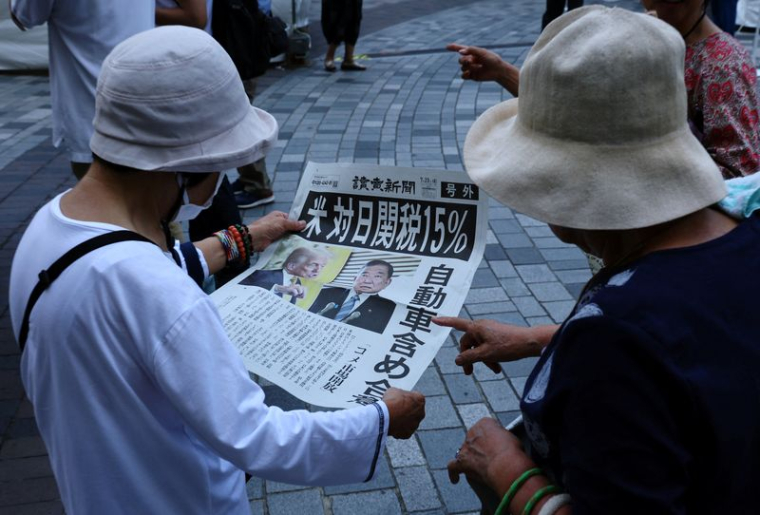 Des personnes réagissent en lisant une édition spéciale du journal Yomiuri Shimbun qui rapporte l'accord tarifaire entre les États-Unis et le Japon, à Tokyo