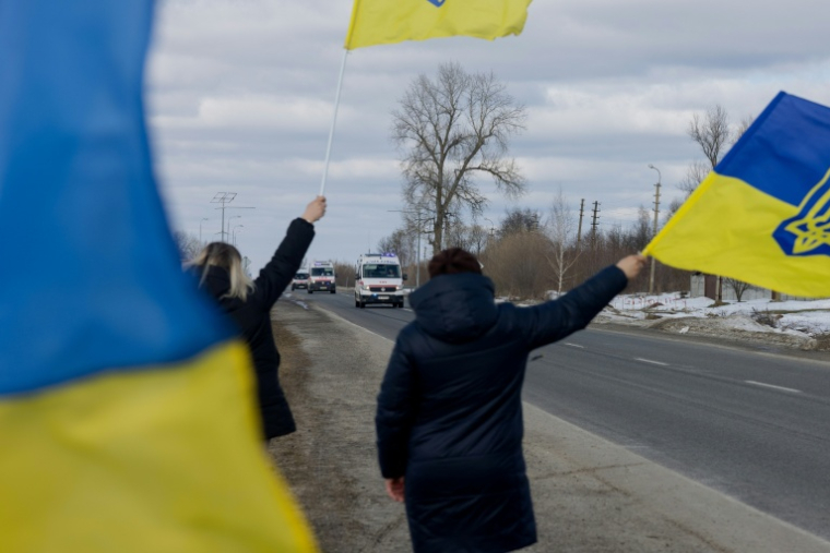 Des personnes agitent des drapeaux sur le bord  d'une route à l'approche d'un convoi de soldats libérés par les Russes après un échange de prisonniers, le 6 mars 2026 dans un lieu non précisé dans le nord de l'Ukraine ( AFP / Tetiana DZHAFAROVA )
