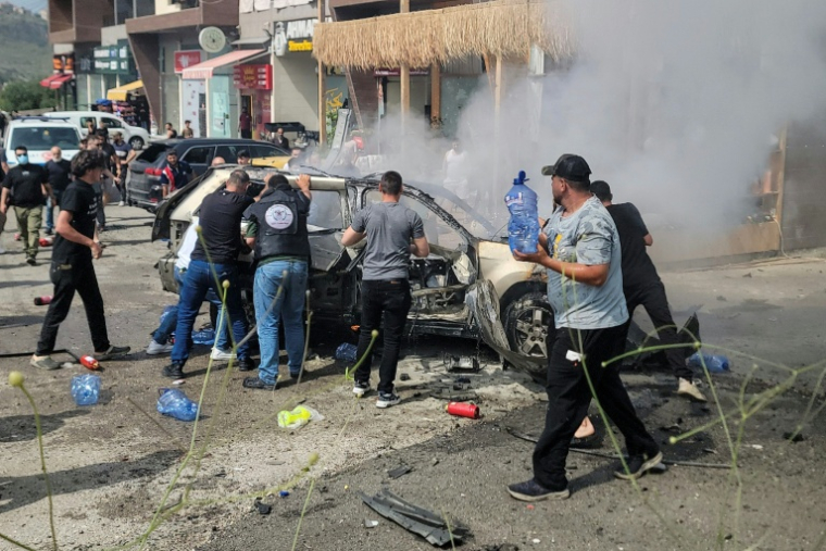 Des secouristes et des passants éteignent un véhicule en feu, cible d'une frappe de drone israélien, dans la ville de Jiyeh, au sud de Beyrouth, le 13 mai 2026 au Liban ( AFP / Fadel ITANI )