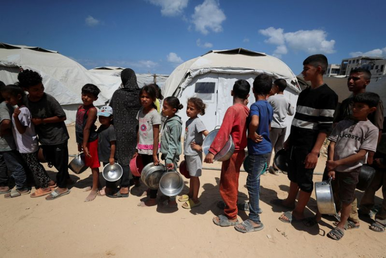 Des Palestiniens attendent de recevoir de la nourriture préparée par une cuisine caritative près des tentes où ils ont trouvé refuge après avoir été déplacés par l'offensive militaire israélienne, à Gaza