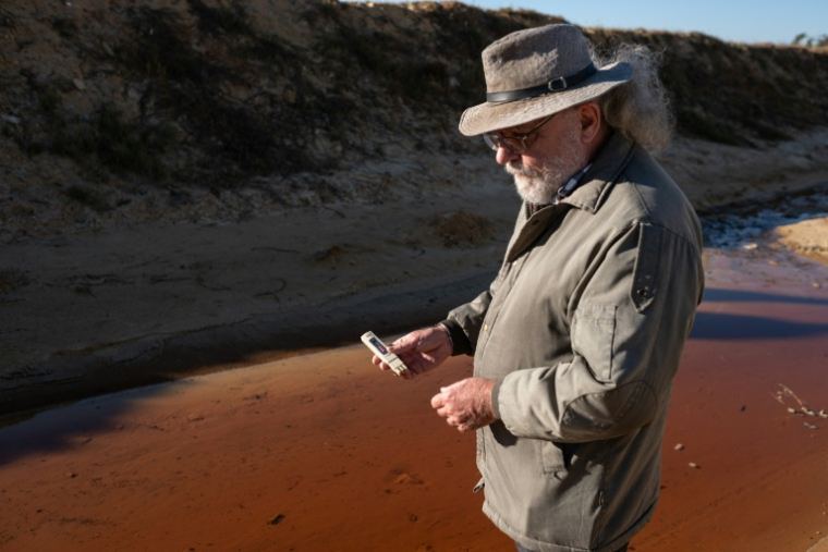 David van Wyk, chercheur principal à la Bench Marks Foundation, effectue des tests dans un cours d'eau à la décharge de la mine de Snake Park, à Soweto, le 30 mai 2025 en Afrique du Sud ( AFP / EMMANUEL CROSET )