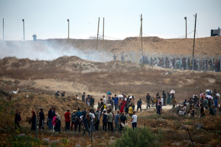 Des Palestiniens déplacés se dirigent vers un centre de distribution d'aide humanitaire, alors que des bombes fumigènes sont tirées par les troupes israéliennes, dans le centre de la bande de Gaza, le 8 juin 2025 ( AFP / Eyad BABA )