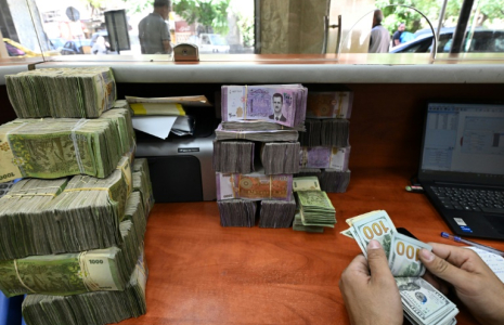 Un employé compte des dollars américains devant une pile de livres syriennes dans un bureau de change à Damas, le 21 mai 2025 en Syrie ( AFP / LOUAI BESHARA )