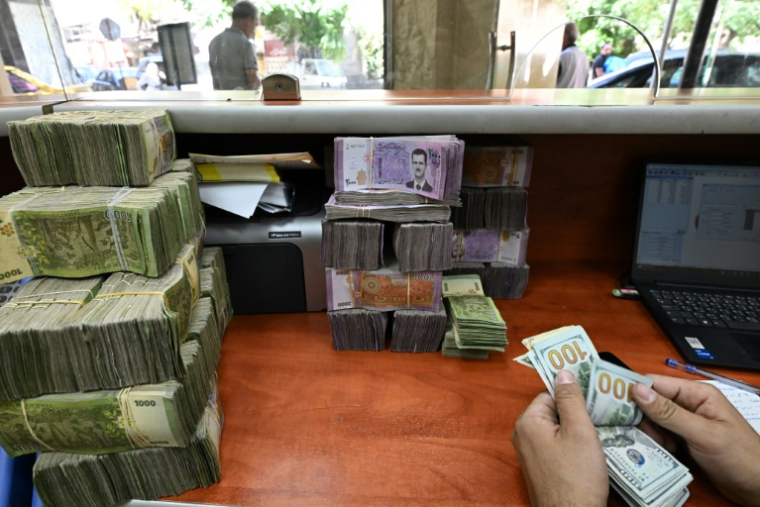 Un employé compte des dollars américains devant une pile de livres syriennes dans un bureau de change à Damas, le 21 mai 2025 en Syrie ( AFP / LOUAI BESHARA )