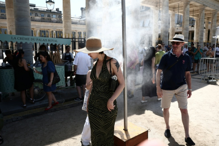 Des piétons se rafraîchissent sous un brumisateur installé par la mairie de Paris pendant une vague de chaleur à Paris, le 21 juin 2026 ( AFP / Guillaume BAPTISTE )
