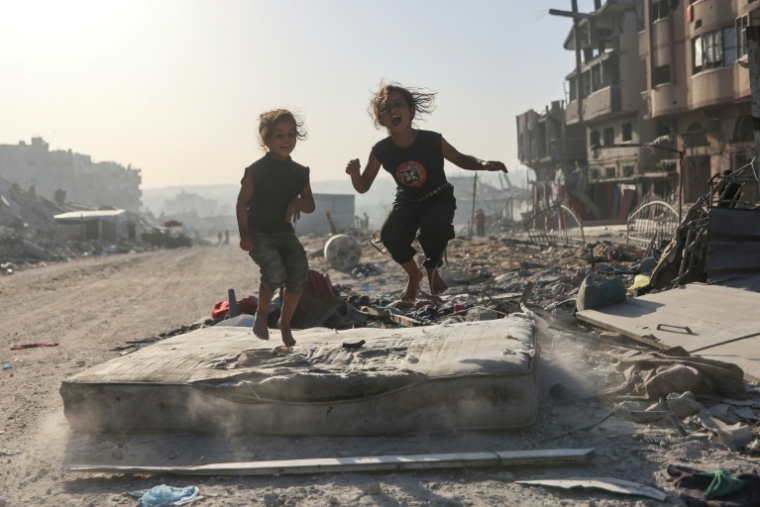 Des fillettes palestiniennes jouent sur un matelas abandonné au milieu des décombres d'immeubles détruits dans le quartier de Cheikh Radwane, à Gaza-ville, le 22 octobre 2025 ( AFP / Omar AL-QATTAA )