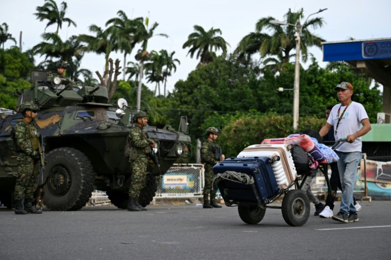 Un homme chargé de valises sur un diable passe devant des militaires colombiens stationnés à Cucuta, à la frontière avec le Venezuela, le 3 janvier 2026  ( AFP / Raul ARBOLEDA )
