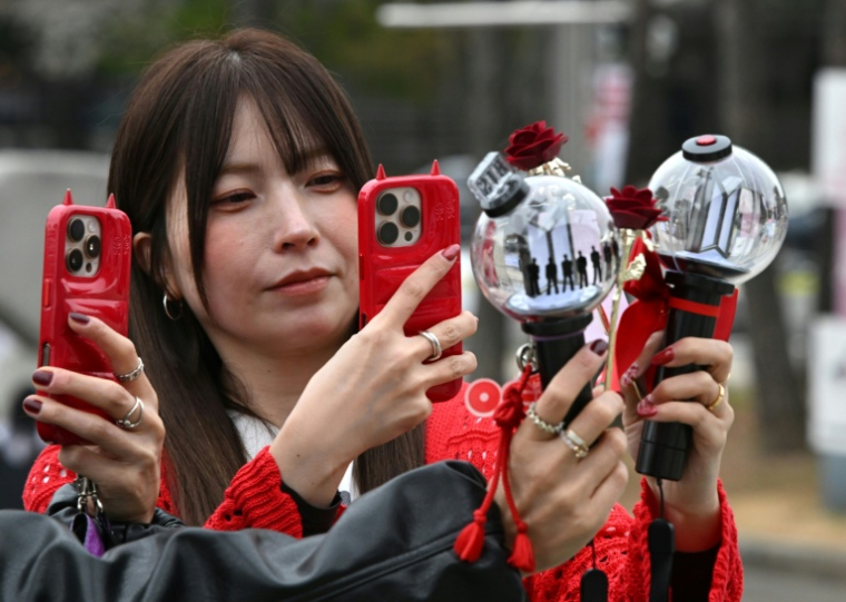 Des fans prennent des photos de bâtons lumineux à l'effigie de BTS à leur arrivée au stade où le groupe de K-pop se produira, à Goyang, le 9 avril 2026 ( AFP / Jung Yeon-je )