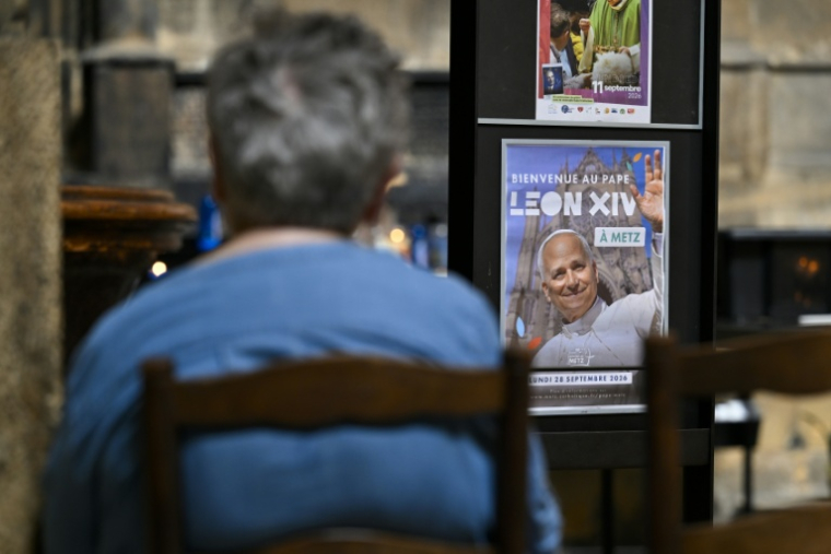 Une personne prie à côté d'une affiche annonçant la venue du pape Léon XIV dans la cathédrale Saint-Etienne de Metz le 3 septembre 2026 ( AFP / Jean-Christophe VERHAEGEN )