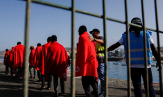 La police Frontex accompagne plusieurs migrants vers une tente de la Croix-Rouge après leur débarquement d'un navire des garde-côtes espagnols, dans le port d'Arguineguin