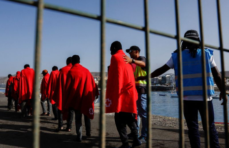 La police Frontex accompagne plusieurs migrants vers une tente de la Croix-Rouge après leur débarquement d'un navire des garde-côtes espagnols, dans le port d'Arguineguin