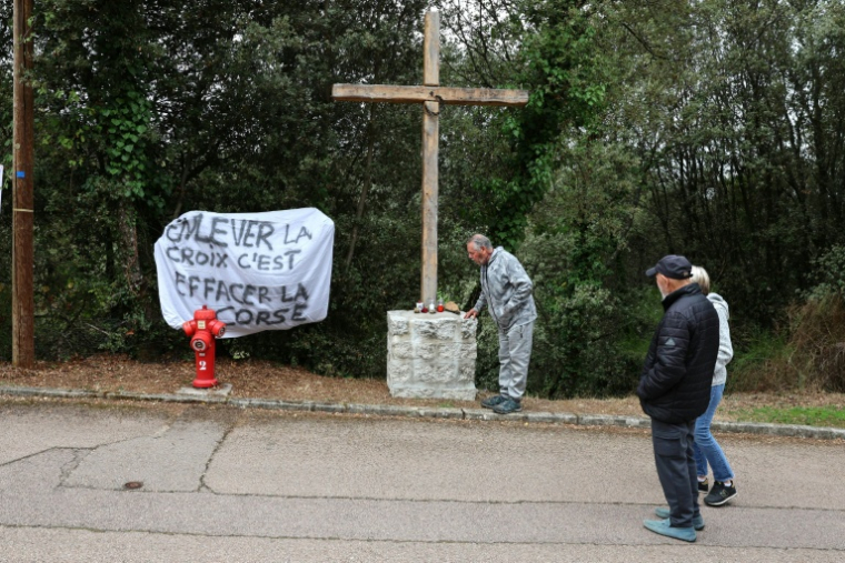 Une banderole à côté d'une croix en bois objet de polémiques à l'entrée du village de Quasquara, le 14 octobre 2025 en Corse-du-Sud ( AFP / Pascal POCHARD-CASABIANCA )