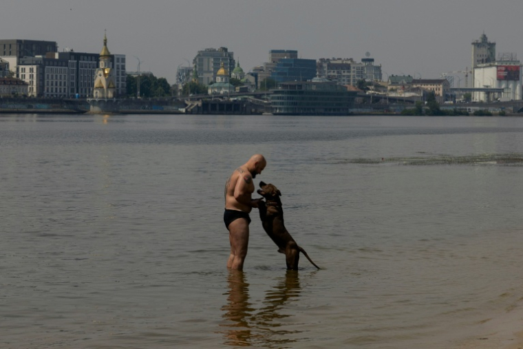 Un homme en maillot de bain joue avec son chien dans l'eau du fleuve Dniepr, à Kiev, en Ukraine, le 29 juin 2026. ( AFP / Tetiana DZHAFAROVA )