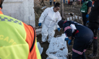 Des membres des services médicaux d'urgence (EMS) écrivent sur un sac mortuaire après avoir trouvé des corps dans une maison après des inondations hivernales, le 12 juin 2025 près de Mthatha, en Afrique du Sud ( AFP / EMMANUEL CROSET )