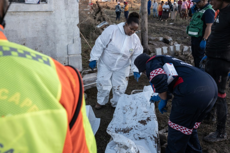 Des membres des services médicaux d'urgence (EMS) écrivent sur un sac mortuaire après avoir trouvé des corps dans une maison après des inondations hivernales, le 12 juin 2025 près de Mthatha, en Afrique du Sud ( AFP / EMMANUEL CROSET )