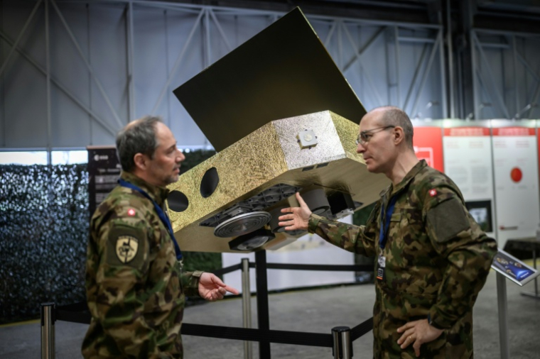 Des officiers de l'armée suisse devant une réplique grandeur nature d'un satellite qui sera bientôt lancé dans l'espace pour détecter, entre autres, les brouilleurs de GPS, à Thoune, en Suisse, le 26 mars 2026 ( AFP / Fabrice COFFRINI )
