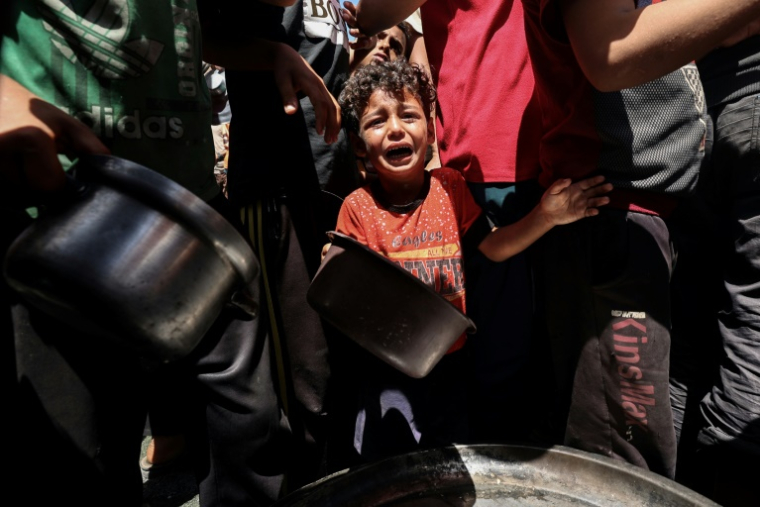 Un enfant pleure au milieu de Palestiniens qui attendent de recevoir un repas chaud distribué par une association caritative locale à Nousseirat, dans le centre de la bande de Gaza, le 24 mai 2025 ( AFP / Eyad BABA )