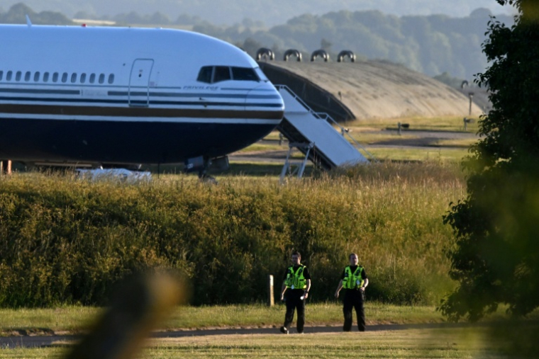 Des  policiers patrouillent près d'un Boeing 767 stationné sur la piste de la base militaire d'Amesbury, à Salisbury, le 14 juin 2022 en Grande-Bretagne, s'aprêtant à transporter des demandeurs d'asile au Rwanda ( AFP / JUSTIN TALLIS )