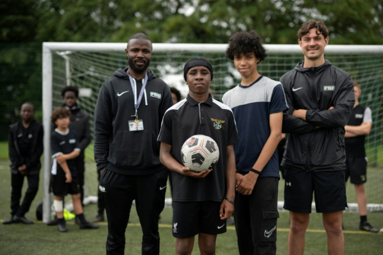 Matt Bishop (d) et Ezektel Agyemang (g), membres du programme "Football Beyond Borders", avec les élèves Fabian Myers (2e d) et Kaziah Cameron (2e g) après un match de foot au collège-lycée public Our Lady and St Chad Catholic Academy, à Wolverhampton, le 12 juin 2026 au Royaume-Uni ( AFP / Oli SCARFF )