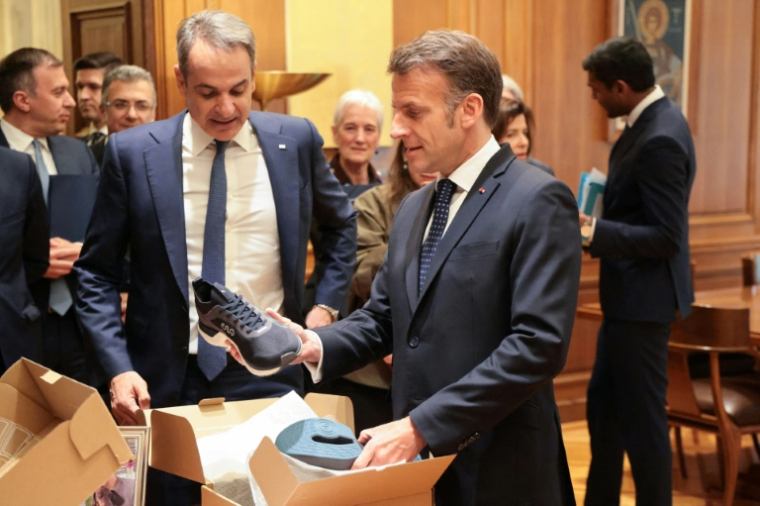 Le président français Emmanuel Macron (D) reçoit des mains du Premier ministre grec Kyriakos Mitsotakis une paire de baskets fabriquées en Grèce à l'issue d'un déjeuner  Athènes, le 25 avril 2026 à Athènes  ( AFP / Ludovic MARIN )