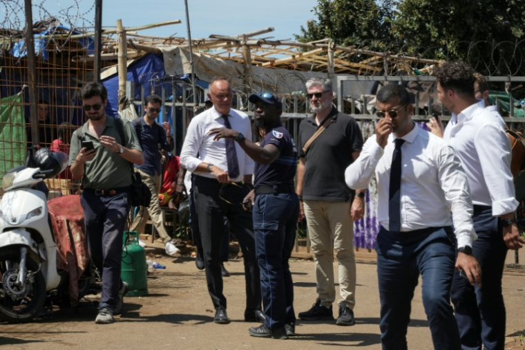 Édouard Philippe (c), fondateur et président du parti Horizons, maire du Havre et candidat à l'élection présidentielle, parle avec un policier devant un camp de réfugiés dans le village de Tsoundzou 2, à Mamoudzou, le 21 août 2026 sur l'île de Mayottte ( AFP / Marine Gachet )
