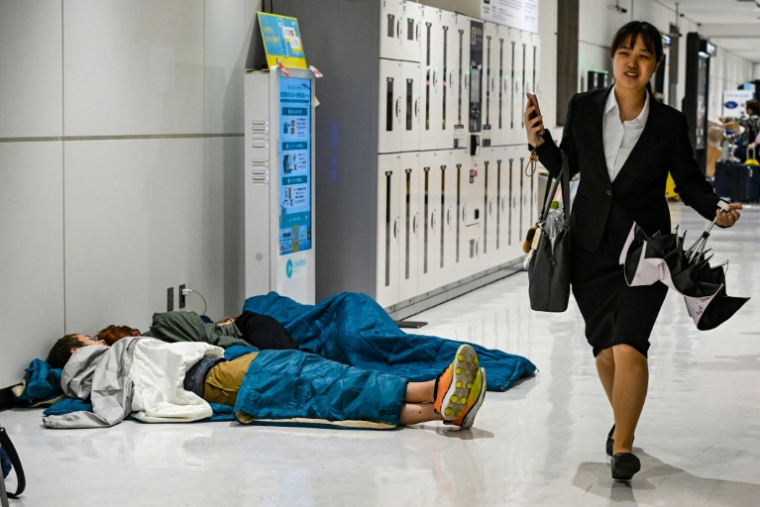 Des passagers dorment à l'aéroport de Narita le 14 août 2026 au Japon ( AFP / Andrew CABALLERO-REYNOLDS )