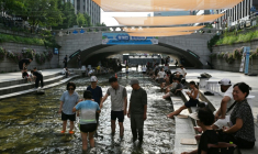 Des personnes se rafraîchissent à l'ombre de pare-soleil au-dessus du ruisseau Cheonggyecheon, à Séoul, le 3 août 2026 ( AFP / GREG BAKER )