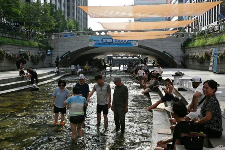 Des personnes se rafraîchissent à l'ombre de pare-soleil au-dessus du ruisseau Cheonggyecheon, à Séoul, le 3 août 2026 ( AFP / GREG BAKER )