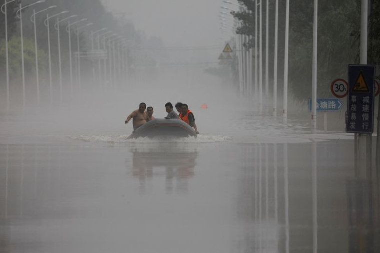 Des gens traversent en bateau une route inondée après les pluies du typhon Doksuri, à Zhuozhou en Chine