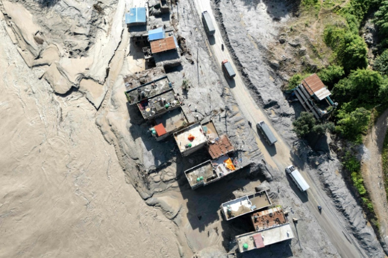 Vue aérienne de véhicules circulant devant des maisons couvertes de boue à la suite de la crue destructrice dans l'Himalaya, le 20 août 2026 soudaines à Baireni, dans le district népalais de Dhading  ( AFP / Manan VATSYAYANA )