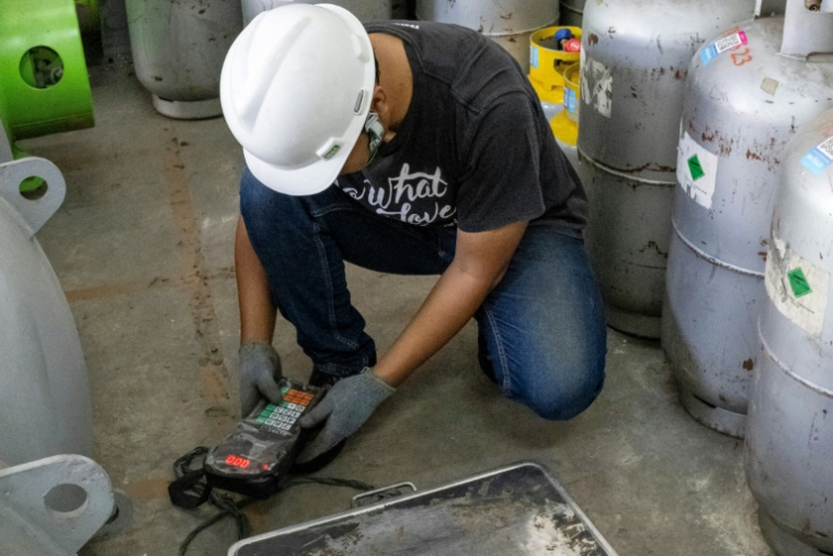 Le technicien Ari Sobaruddin de la société Recoolit vérifie le gaz réfrigérant stocké dans des bouteilles dans l'entrepôt de l'entreprise à Jakarta, le 12 juin 2025 en Indonésie ( AFP / Bay ISMOYO )