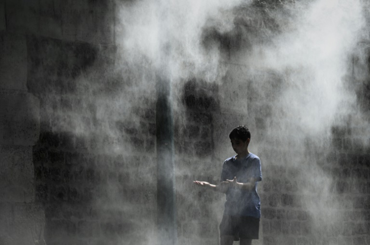 Un jeune garçon profite d'un brumisateur installé sur un quai de la Seine à Paris lors d'une canicule, le 25 juillet 2019 ( AFP / PHILIPPE LOPEZ )