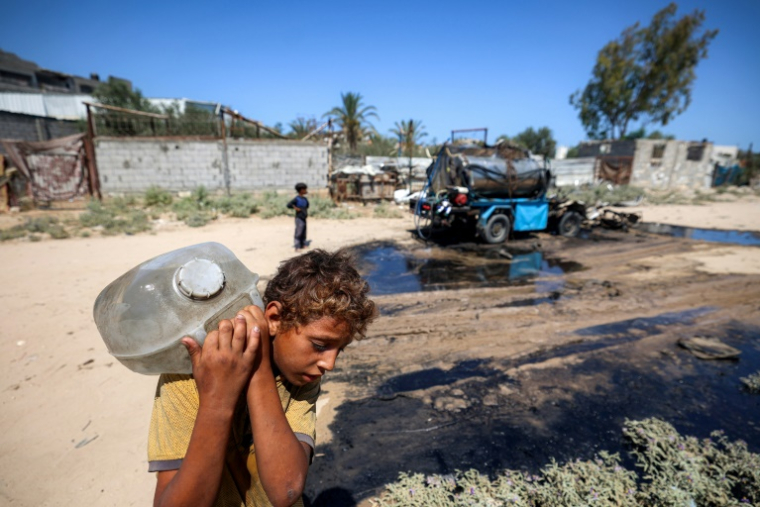 Un garçon porte un jerrycan rempli d'eau prise d'une citerne touchée par un bombardement israélien dans le camp de Nousseirat, dans le centre de la bande de Gaza, le 14 juillet 2025 ( AFP / Eyad BABA )