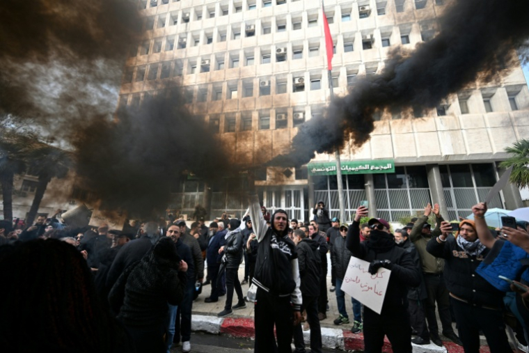 Un manifestant allume un fumigène noir devant le siège d'une entreprise accusée de pollution, lors d'une marche "contre les injustices" dénonçant le recul des libertés et du niveau de vie à Tunis, le 22 novembre 2021 ( AFP / FETHI BELAID )