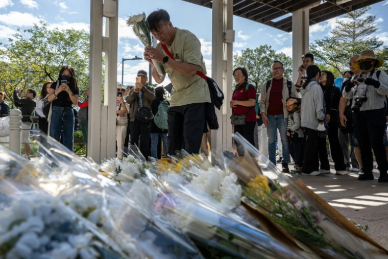 Des personnes se rassemblent le 29 novembre 2025 pour déposer des fleurs devant le complexe résidentiel de Wang Fuk Court à Hong Kong à la suite de l’incendie meurtrier survenu trois jours auparavant ( AFP / Philip FONG )